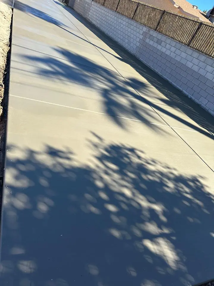 In Buckeye, AZ, the shadow of a tree dances on freshly poured concrete, laid by skilled concrete contractors. A block wall and wooden fence run parallel on one side, creating an intriguing pattern on the smooth gray surface.